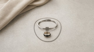 Corrente, bracelete e anel masculinos discretos da Una sobre fundo bege e cinza