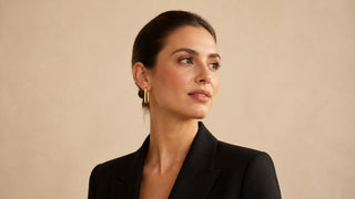 Mulher usando argola reta dourada com blazer preto em fundo bege