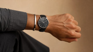Homem usando relógio preto e bracelete prateado no mesmo pulso