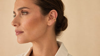 Mulher usando ear cuff dourado com brinco pequeno em composição equilibrada