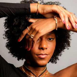 Mix de anéis e pulseiras douradas da UNA Semijoias em composição fashion feminina, com fundo neutro e styling sofisticado