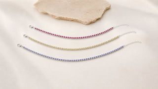 Três pulseiras riviera coloridas rosa, amarela e lilás da Una sobre fundo marfim