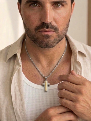Colar de aço masculino da UNA com cruz prateada e detalhe dourado, acessório sofisticado em fundo neutro
