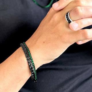 Pulseira masculina em aço inox black com zircônias verdes estilo esmeralda da UNA Semijoias no pulso masculino, combinada a anéis em aço, em foto de lifestyle.