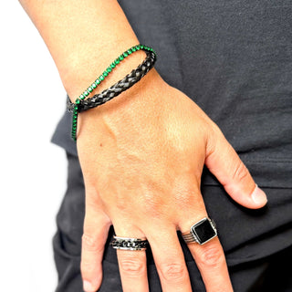 Pulseira masculina em aço inox black com zircônias verdes da UNA Semijoias no pulso em close, combinada a anéis escuros, em fundo claro e look casual.