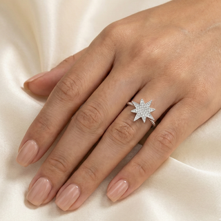 Anel estrela cadente cravejado banhado a prata 925 da UNA Semijoias em fundo branco, com centro em forma de estrela de oito pontas em destaque na mão de uma modelo.