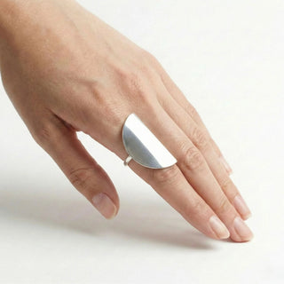 Anel regulável chapa metade oval banhado a prata 925 da UNA Semijoias em fundo branco, com design minimalista e polido na mão de uma modelo.