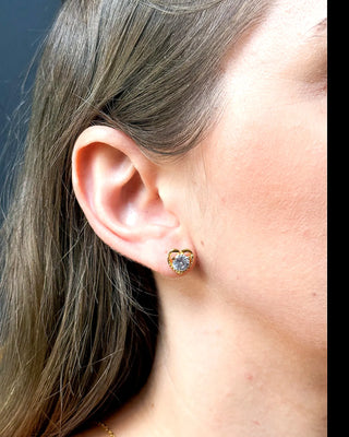 Brinco coração cravejado banhado a ouro 18k da UNA Semijoias na orelha feminina em close lateral, com pedra em forma de coração em destaque.