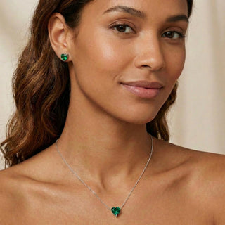 Brinco coração verde banhado a prata 925 da UNA Semijoias na orelha feminina, foto lifestyle com colar combinando, fundo neutro.