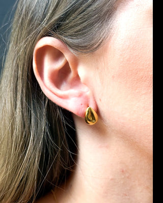 Brinco em formato de gota banhado a ouro 18k da UNA Semijoias e Aço na orelha feminina, em close lateral, com acabamento polido em destaque.