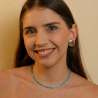 Choker riviera azul banhada a prata 925 da UNA Semijoias no colo feminino em close, valorizando o brilho das pedras rosas ao redor do pescoço.