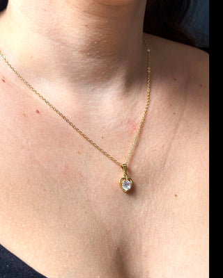 Colar coração cravejado banhado a ouro 18k da UNA Semijoias no colo feminino em close, com pingente em forma de coração com pedra central em destaque.