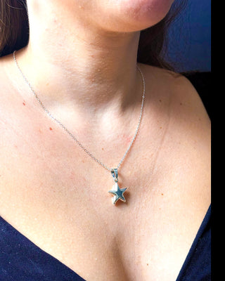 Colar estrela banhado a prata 925 da UNA Semijoias no colo feminino em close, com pingente de estrela lisa em destaque.