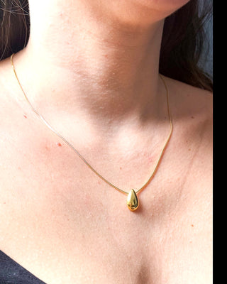 Colar delicado com pingente em formato de gota banhado a ouro 18k da UNA Semijoias no colo feminino, em fundo neutro, com corrente fina em destaque.