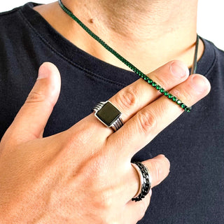 Colar masculino em aço inox black com pedras verde-esmeralda da UNA Semijoias em close na mão do modelo, mostrando brilho e acabamento fino.