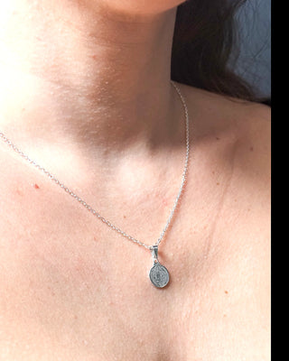 Colar São Bento banhado a prata 925 da UNA Semijoias no colo feminino em close, com medalha religiosa delicada em destaque.