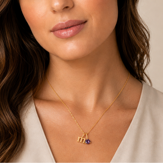 Colar Sign letra M com ponto de luz ametista banhado a ouro 18k da UNA no colo feminino, em close editorial delicado.