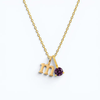 Colar Sign letra M com ponto de luz ametista banhado a ouro 18k da UNA em fundo neutro, com inicial e pedra em destaque.