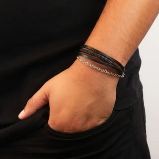 Pulseira de aço com couro preto e corrente da UNA, modelo unissex com design sofisticado em close no pulso masculino
