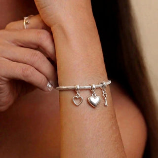 Pulseira berloque tradicional banhada a prata 925 da UNA no pulso feminino, com berloques de coração e chave em foto editorial