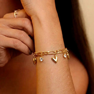 Pulseira coração banhada a ouro da UNA no pulso feminino, com pingentes delicados e design sofisticado em close
