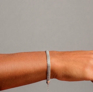 Pulseira corrente de tela banhado a ródio da UNA Semijoias no pulso feminino, em composição sofisticada com fundo neutro