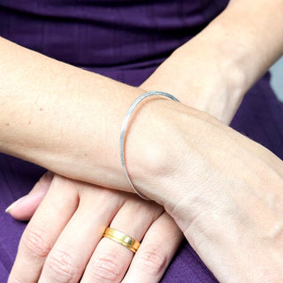 Pulseira fita banhada a prata minimalista no pulso feminino, UNA Semijoias, em look com vestido roxo.