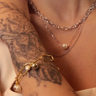 Pulseira com pérola barroca e bola banhada a ouro 18k da UNA no pulso feminino, com design sofisticado em foto editorial