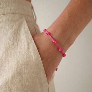 Pulseira verão nozinho da sorte rosa da UNA Semijoias no pulso feminino, em close lateral, combinada com look claro e casual de verão.