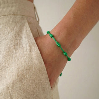 Pulseira verão nozinho da sorte verde da UNA Semijoias no pulso feminino, em close lateral, combinada com look claro e casual de verão.